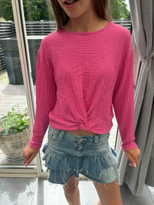 Rosa långärmad topp med knut - Säljer en rosa långärmad topp med twistad knut framtill. Toppen har en strukturerad yta och rund halsringning. Perfekt till jeans eller kjol för en trendig look.