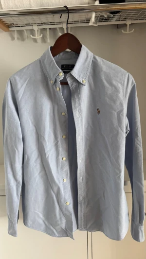 Ljusblå skjorta från Ralph Lauren - Klassisk ljusblå skjorta från Ralph Lauren med button-down krage och broderad logga på bröstet. Skjortan har lång ärm, vita knappar framtill och är tillverkad i mjuk bomull.              Säljer då den inte passar mig.                                                        Skriv gärna vid frågor!