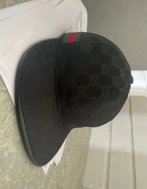 Svart keps från Gucci med monogram - Snygg svart keps från Gucci med klassiskt GG-monogram över hela kepsen och en grön-röd rand på sidan. Kepsen har böjd skärm och är tillverkad i ett slitstarkt material som ger en exklusiv känsla. Perfekt för dig som vill ha en stilren accessoar med lyxig touch.