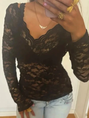 Svart spetsblus med v-ringning - Snygg svart långärmad blus i spets med v-ringad hals och transparent design. Blusen har ett blommigt spetsmönster och sitter tight mot kroppen. Perfekt att styla med jeans eller kjol för en trendig look. Se lagning på baksidan på sista bilden 
