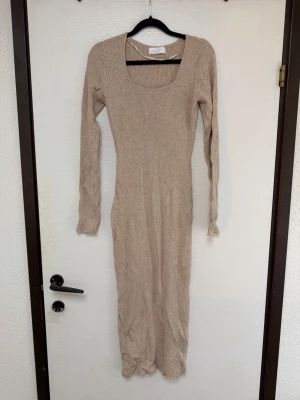 Beige ribbad långklänning  - Snygg beige långklänning med ribbad struktur och lång ärm. Klänningen har en djup, fyrkantig ringning och är figurnära i modellen. Perfekt för dig som gillar stilrena och enkla plagg med en modern touch. ( tänk på jag har hund i hemmet) 