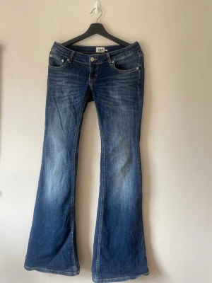 Blå bootcut jeans Blaze från 157  - Ett par klassiska blå bootcut jeans från 157 med snygg slitning framtill. Jeansen har fickor, låg midja och utsvängda ben. Tillverkade i mjuk denim med kontrastsömmar och knappgylf. Perfekta för en avslappnad och trendig look.