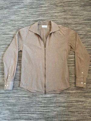 Beige overshirt John Henric - Stilren beige overshirt från John Henric med dragkedja framtill och klassisk krage. Långärmad modell med breda manschetter och vita knappar. Tillverkad i ett mjukt tyg som ger en avslappnad men ändå snygg look.