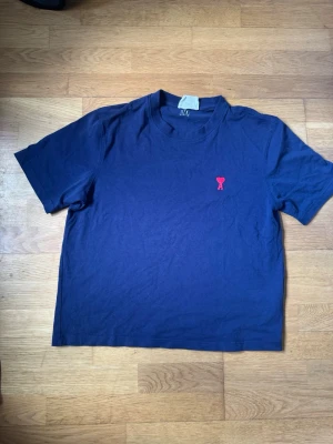 Mörkblå t-shirt från Ami Paris - Snygg mörkblå t-shirt från Ami Paris med klassisk passform och korta ärmar. På bröstet finns Ami:s ikoniska röda hjärta med A broderat. Tillverkad i mjuk bomull som känns skön mot huden. Perfekt till jeans eller shorts.