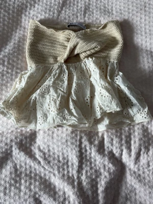 Beige virkad och broderad tubtopp - Supersöt beige tubtopp med virkad överdel och broderad, volangig nederdel. Toppen har ett twistat parti framtill och fina hålbroderier på tyget. Perfekt för sommaren.