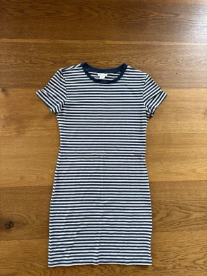 Randig kortklänning från H&M - Säljer en randig kortklänning från H&M med marinblå och vita ränder. Klänningen har rund halsringning, korta ärmar och är gjord i mjuk bomull. Perfekt för en avslappnad och stilren look.