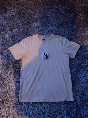 Beige NY t-shirt från '47 Brand - Snygg beige t-shirt från '47 Brand med klassisk NY-logga och broderad röd ros på bröstet. T-shirten har rund hals och korta ärmar, perfekt för en clean och stilren look. Tillverkad i mjuk bomull för skön komfort.