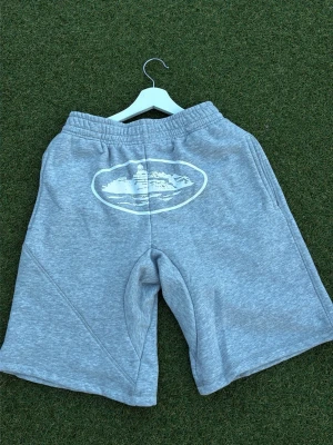 Grå sweatshorts med tryck - Gråa sweatshorts med vitt tryck framtill, elastisk midja och avslappnad passform. Perfekta för chill dagar eller när du vill ha det bekvämt. Mjukt material och klassisk look.