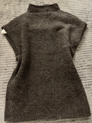 Mörkbrun stickad väst Gina Tricot - Mysig mörkbrun stickad väst från Gina Tricot i ullblandning. Modellen har hög krage och är ärmlös, perfekt att styla över en skjorta eller tröja. Enkel och stilren design som passar till många outfits.