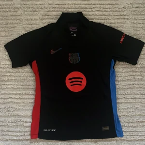 FC Barcelona matchtröja Raphinha 11 - Snygg svart FC Barcelona matchtröja från Nike med Raphinha 11 på ryggen. Tröjan har röda och blå detaljer på sidorna, Spotify-logga på bröstet och klubbmärke. Tillverkad i lätt och ventilerande material med Dri-FIT-teknologi.