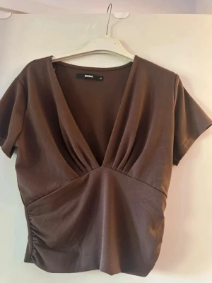 Brun omlottopp från Bik Bok - Snygg brun topp från Bik Bok med djup v-ringning och korta ärmar. Köpt för något år sedan, använd fåtal gånger. Storlek M
