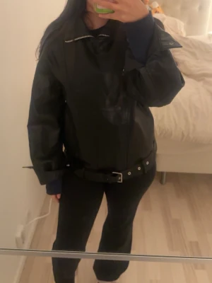 Oversized svart skinnjacka med bälte - Säljer en helt ny svart oversized skinnjacka med coolt bälte i midjan och dragkedja framtill. Jackan har breda axlar, klassisk bikerstil och detaljer. Den är i storlek XS men passar även S/M. 