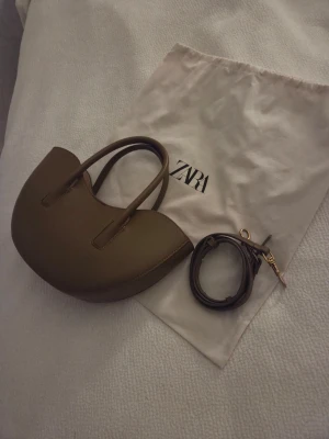 Oval mini shoppingbag från Zara - Jättefin mini shoppingväska med axelband och handtag, även med en liten plånbok med dragkedja i. Helt ny och kommer med dustbag! Köpt för 500kr, sista pris 300kr✨🫶🏻