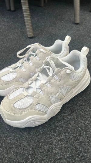 Vita Nike sneakers i mocka och mesh - Säljer ett par vita Nike sneakers med cool design. Skorna har ovandel i mocka och mesh för en fräsch look och bra andningsförmåga. Tjock sula och klassisk Nike Swoosh på sidan. Perfekta för dig som gillar stilrena och sportiga sneakers.