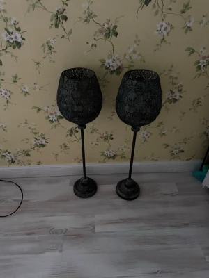 Två höga metalllyktor i svart - Säljer två dekorativa höga lyktor i svart metall med snyggt mönstrat utskuret mönster. Perfekta som ljushållare eller för att skapa mysig stämning i rummet. Lyktorna har rund fot och kupolformad topp.