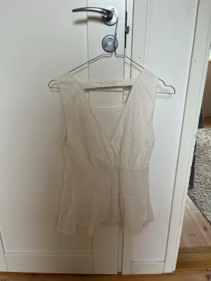 Vit topp med spets och volang - Säljer en superfin vit topp med spetsdetaljer upptill och volang nedtill. Toppen är använd fåtal gånger och är i bra skick. Superfin till sommaren, skriv ifall fler frågor!🩷🩷🩷