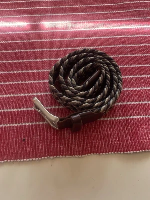 Flätat brunt bälte från Jack & Jones - Snyggt beige, vit och svart flätat bälte! 90 cm långt och köpt från Jack and Jones! Bältet är i fint skick bara att den blivit lite färgad på insidan av ett par mörkblåa jeans och lite färg borta från metallen men inget av det syns! Nypris 300! Kan gå ner lite 