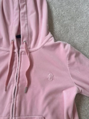 Ljusrosa velour hoodie från Juicy Couture - Säljer en ljusrosa hoodie i mjuk velour från Juicy Couture. Hoodien har dragkedja, huva med snören och en liten broderad logga på bröstet. Perfekt för en chill och trendig look. Betalning via vanlig swish! 