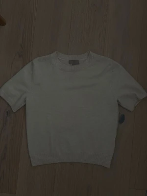 Creme vit stickad tröja från H&M - Kortärmad stickad tröja i beige färg från H&M. Tröjan har rund halsringning och ribbade kanter vid ärmslut och nederkant. Perfekt för lager på lager och enkel att matcha med olika stilar.