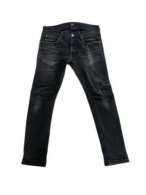 Svarta slim jeans från Lee modell Luke  - Säljer ett par svarta slim jeans från Lee med slitningar och snygg tvättad look. Jeansen har fem fickor, dragkedjegylf och silverfärgade detaljer. Perfekta för dig som gillar en trendig och avslappnad stil. Mycket bra pris. Modellen heter Luke. 