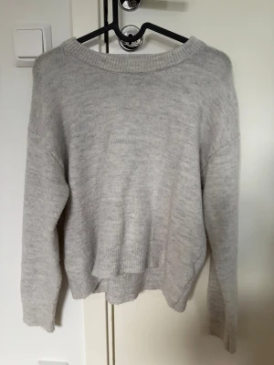 Ljusgrå stickad tröja Gina Tricot - Ljusgrå stickad tröja från Gina Tricot med avslappnad passform och bred ribbad halsringning. Tröjan har långa ärmar och ribbade muddar vid ärmslut och nederkant. Perfekt att styla med jeans eller kjol för en enkel look.