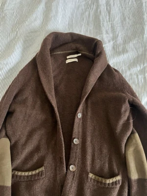 Brun kofta från Massimo Dutti - Brun kofta i ull, angora och kashmir från Massimo Dutti. Koftan har stora knappar, två fickor framtill och snygga mockadetaljer på armbågar och fickor. 