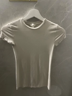 Beige basic t-shirt från H&M - En stilren beige t-shirt från H&M med rund halsringning och korta ärmar. Modellen är figurnära och passar perfekt till jeans eller kjol. 