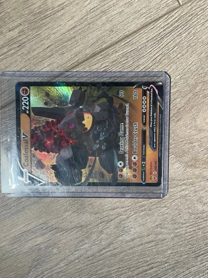 Pokémonkort Colossal V holografisk - Säljer ett Pokémonkort med Colossal V-motiv. Kortet är holografiskt och har färger i svart, orange och rött. Det ligger i ett genomskinligt plastfodral. Perfekt för samlare eller Pokémonfans.