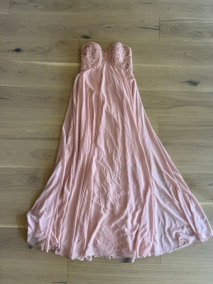 Rosa balklänning - Säljer en balklänning jag aldrig använt, axelbandslös och jättefina detaljer vid bysten. Knyte bak i ryggen, står storlek 38 på lappen skulle säga att den passar S-M. Man kan lägga till axelband(bild 5,6) och kommer även en sjal till💓