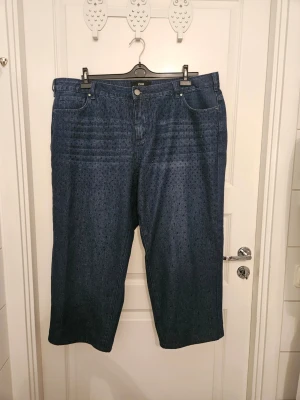 Vida jeans med strass från Zizzi - 1 par mörkblå vida och raka jeans med blå strass från Zizzi. Jeansen är kortade och innerbenslängden är 64 cm. Storlek 48