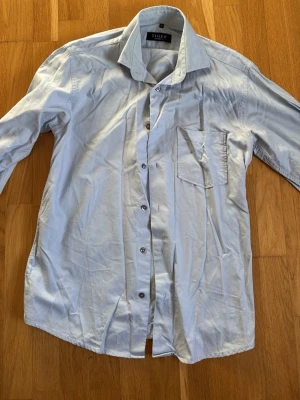 Ljusblå skjorta Tiger of Sweden - Snygg ljusblå skjorta från Tiger of Sweden med klassisk krage och bröstficka. Skjortan har knappar framtill och är långärmad. Tillverkad i mjuk bomull som känns skön mot huden. Perfekt för en clean och stilren look.