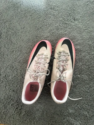 Nike Air Zoom Mercurial rosa/svart - Säljer ett par Nike Air Zoom Mercurial fotbollsskor i ljusrosa med svart swoosh och detaljer. Skorna har snörning, låg profil och en grym yttersula för bra grepp på planen. Snygg färgövergång till rosa vid sulan och cool design på sidan.