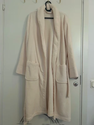 Ljusbeige fluffig morgonrock från Miomare - Mysig ljusbeige morgonrock i mjukt och fluffigt material från Miomare i storlek S 36/38. Har två stora fickor framtill, skärp i midjan och breda muddar vid ärmsluten. Aldrig använd.