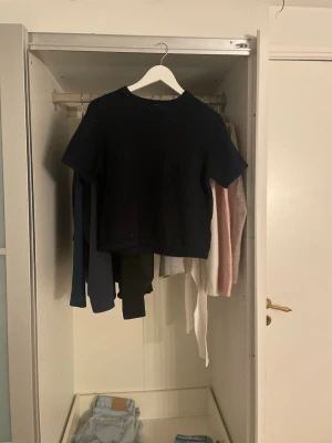 Svart croppad stickad topp - En svart croppad stickad topp med korta ärmar och rund hals. Perfekt för att styla med höga jeans eller kjol. Enkel och stilren design som passar till många olika looks.