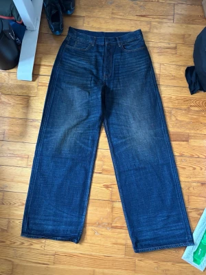 Mörkblå wide leg acne studios jeans - Säljer ett par mörkblå jeans med breda ben och klassisk femficksmodell. Jeansen har en lätt tvättad look med subtila slitningar framtill och bakfickor. Materialet är kraftig denim i bomull. Perfekta för en avslappnad och trendig stil.