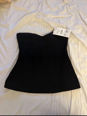 Svart axelbandslös korsett  - Snygg svart axelbandslös korsett från Zara med en figurnära passform och lätt hjärtformad urringning. Toppen har en stilren design och är perfekt att styla med både jeans och kjol. Materialet är mjukt och stretchigt för extra komfort.