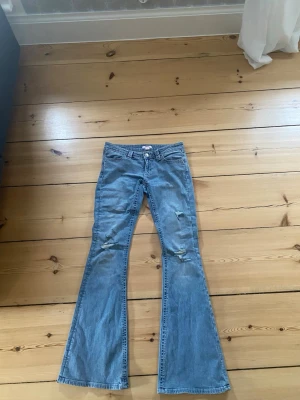Blå bootcut jeans med slitningar - Säljer ett par blåa lågmidjade bootcut jeans. Detaljer på fickorna. Storlek s tall från Gina 14+ helt oanvända