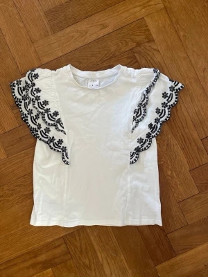 Vit topp med broderade volangärmar  - Supersöt vit topp från Zara med breda volangärmar dekorerade med blått broderi i blommigt mönster.