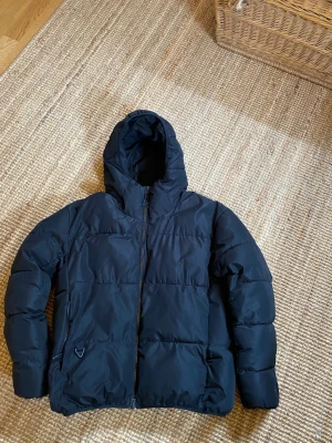 Svart pufferjacka från ZARA - Snygg svart pufferjacka från ZARA med huva och dragkedja framtill. Jackan har två sidofickor och en innerficka med dragkedja. Perfekt för kalla dagar tack vare den tjocka vadderingen och den klassiska pufferlooken. Priset är diskuterbart skriv ifall ni har några frågor.