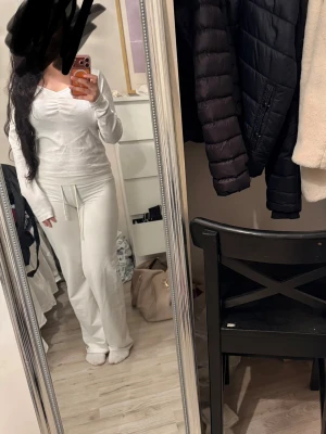 Vit långärmad tröja med dragsko - Säljer en vit långärmad tröja med v-ringning och dragsko i midjan. Tröjan har en avslappnad passform och är perfekt för en chill och bekväm stil. Materialet ser mjukt och stretchigt ut, vilket gör den skön att bära hela dagen. Med prislapp