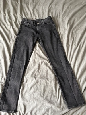 Svarta raka jeans med fem fickor - Säljer ett par svarta jeans med klassisk femficksdesign och raka ben. Jeansen har normal midja och stängs med knapp och dragkedja. Materialet är denim i bomull och de har en enkel, stilren look som passar till det mesta.