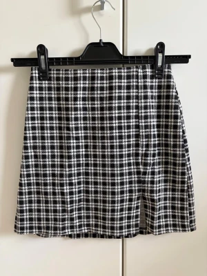 Svartvit rutig minikjol från H&M Divided - Snygg svartvit minikjol från H&M Divided med klassiskt rutigt mönster. Kjolen har en rak passform med liten slits och är perfekt för dig som gillar en stilren och trendig look. 