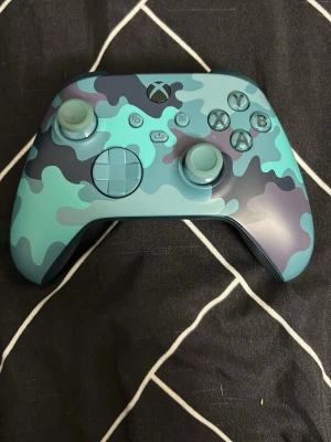 Xbox handkontroll blå camo - Snygg Xbox handkontroll med blått camouflagemönster. Kontrollen har klassisk Xbox-design med två styrspakar, styrkors och ABXY-knappar. Tillverkad i tålig plast och passar perfekt för gaming på Xbox eller PC.