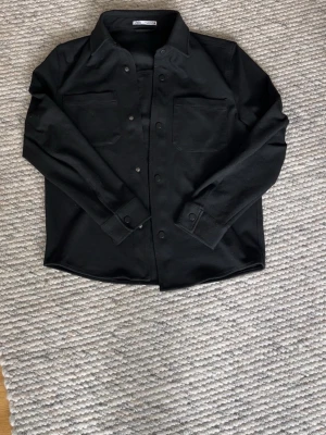 Svart overshirt från Zara - EXTREMT snygg och stilren svart overshirt från Zara med två bröstfickor och knäppning framtill. Klassisk krage och raka ärmar med knapp vid ärmslut. Perfekt lager-på-lager-plagg i ett mjukt, lite tjockare material. Hör av dig med funderingar eller prisförslag 🤩