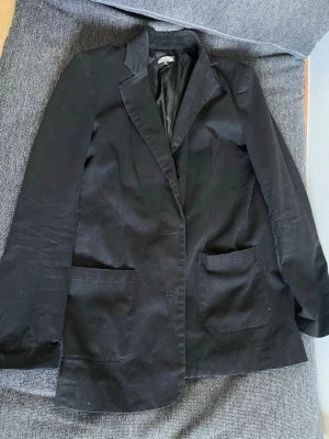 Bikbok Svart kavaj med fickor - Stilren svart kavaj med två stora framfickor och klassisk krage. Kavajen har en rak passform och är helfodrad med blankt innerfoder. Perfekt för en snygg och enkel look.