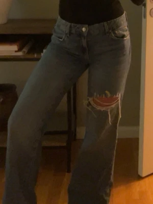 Blåa raka jeans med hål - Säljer ett par blåa raka jeans med stort slitet hål på ena låret.