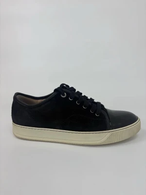 Svarta Lanvin sneakers med lackad tå - Stilrena svarta sneakers med vit sula och snygg lackad tå. Ovandelen är i mocka och skon har svarta skosnören och metallöljetter. Perfekt för dig som gillar en clean och modern look med en twist.