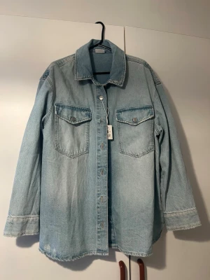 Ljusblå  jeansjacka - Snygg ljusblå jeansjacka med klassisk krage och två bröstfickor med lock och knapp. Jackan har långa ärmar och knäppning framtill med metallknappar. Perfekt för en avslappnad streetstyle-look.