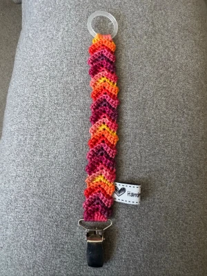 Virkad napphållare - Virkad, flerfärgad napphållare,  irött/orange/gult/lila. Virkad av mig i 100% bomullsgarn med metallclip och silikonring.  Mönsterskapare: animo.design