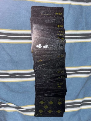 Svart kortlek med gulddetaljer - Säljer en unik kortlek med svarta spelkort och guldfärgade symboler. Baksidan har ett glansigt, ormliknande mönster som ger en lyxig känsla. Perfekt för pokerkvällar eller samlare som vill ha något annorlunda i sin samling.